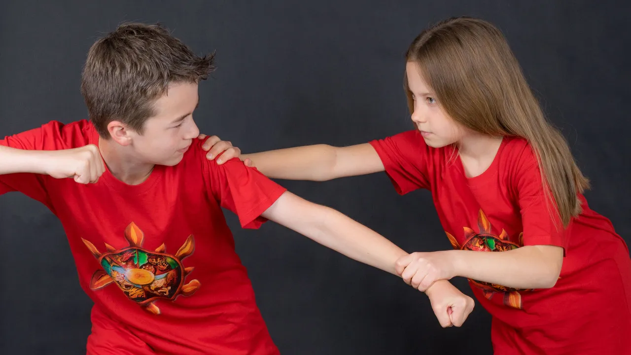 Ein deutlich größerer Junge schlägt zu — das Mädchen fängt seinen Arm ab und hält ihn sicher fest.